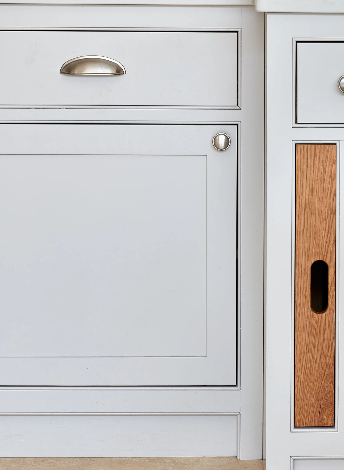 Close-up of kitchen cabinets showcasing a combination of white and wood finishes. A silver handle is attached to the top drawer, while the lower cabinet door features a round silver knob and the adjacent panel displays a vertical wood accent with a black rectangular cutout.