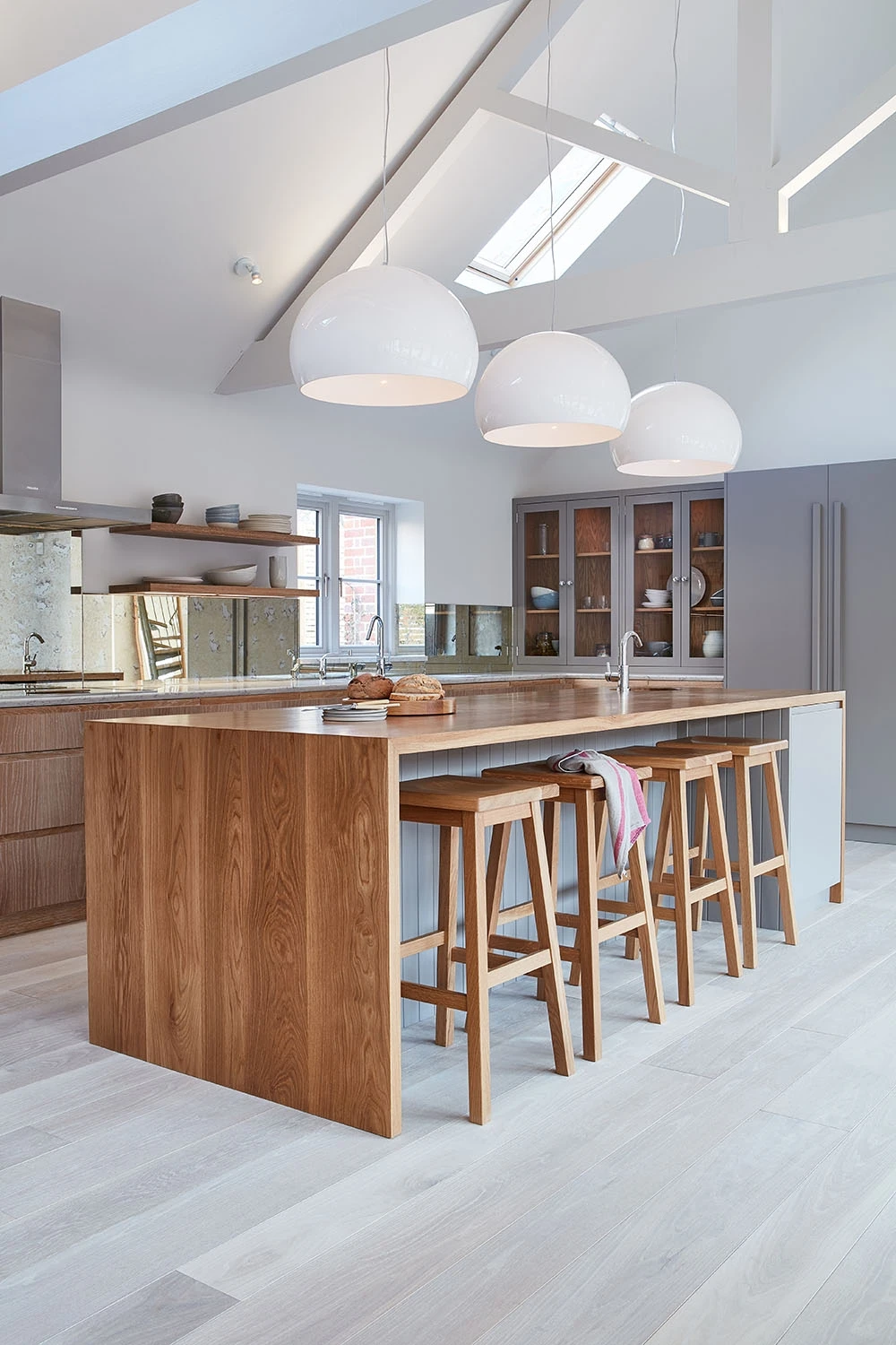 Walnut and grey kitchen with j-groove doors and some glazed wall cabinetry. A central island has v-groove paneling under the walnut worktop