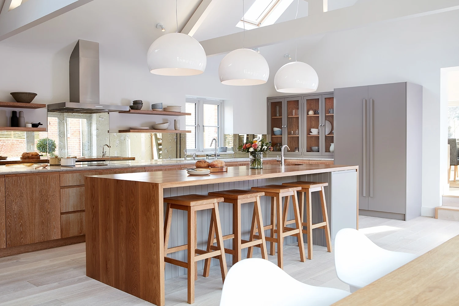 Walnut and grey kitchen with j-groove doors and some glazed wall cabinetry. A central island has v-groove paneling under the walnut worktop