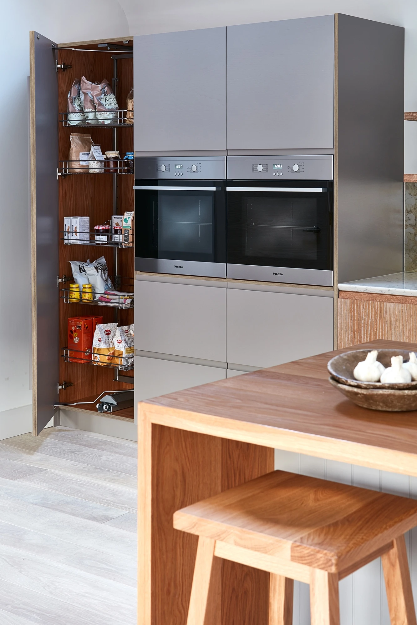 Walnut and grey kitchen with j-groove doors and some glazed wall cabinetry. A central island has v-groove paneling under the walnut worktop