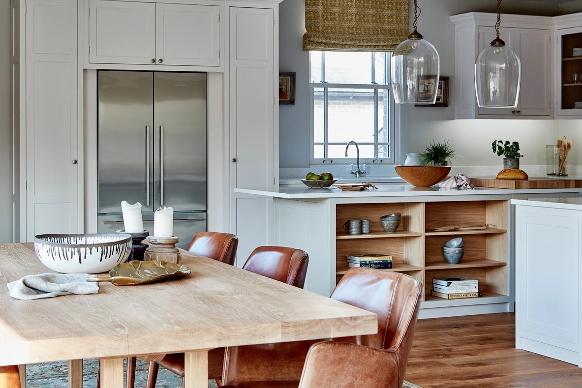  An inviting glimpse into the Hertfordshire Manor kitchen, featuring Shaker cabinets in a warm white hue, oak accents, and ample natural light. A spacious island with a generous seating area anchors the kitchen, creating a sociable and inviting space for family and friends.