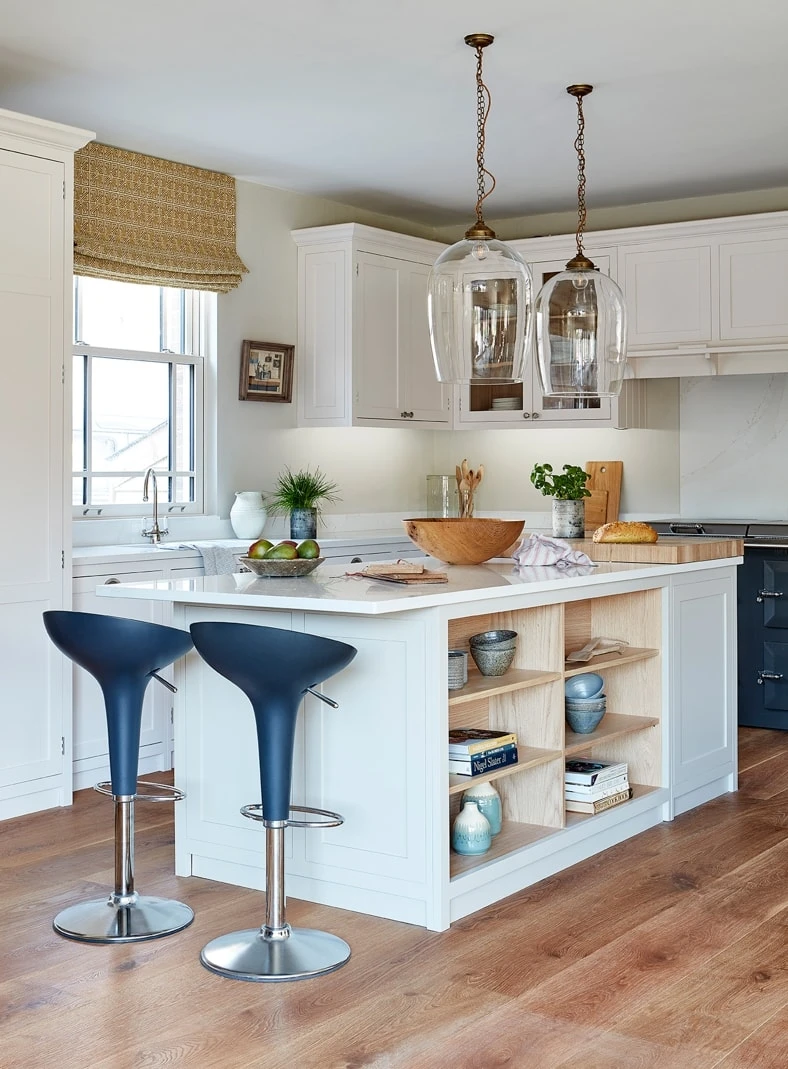 A captivating angle of the Hertfordshire Manor kitchen, showcasing the open shelving and glass-fronted cabinets that showcase curated pieces and add a touch of charm. White Shaker cabinets form the classic backdrop, while the open shelving adds a sense of lightness and airiness.