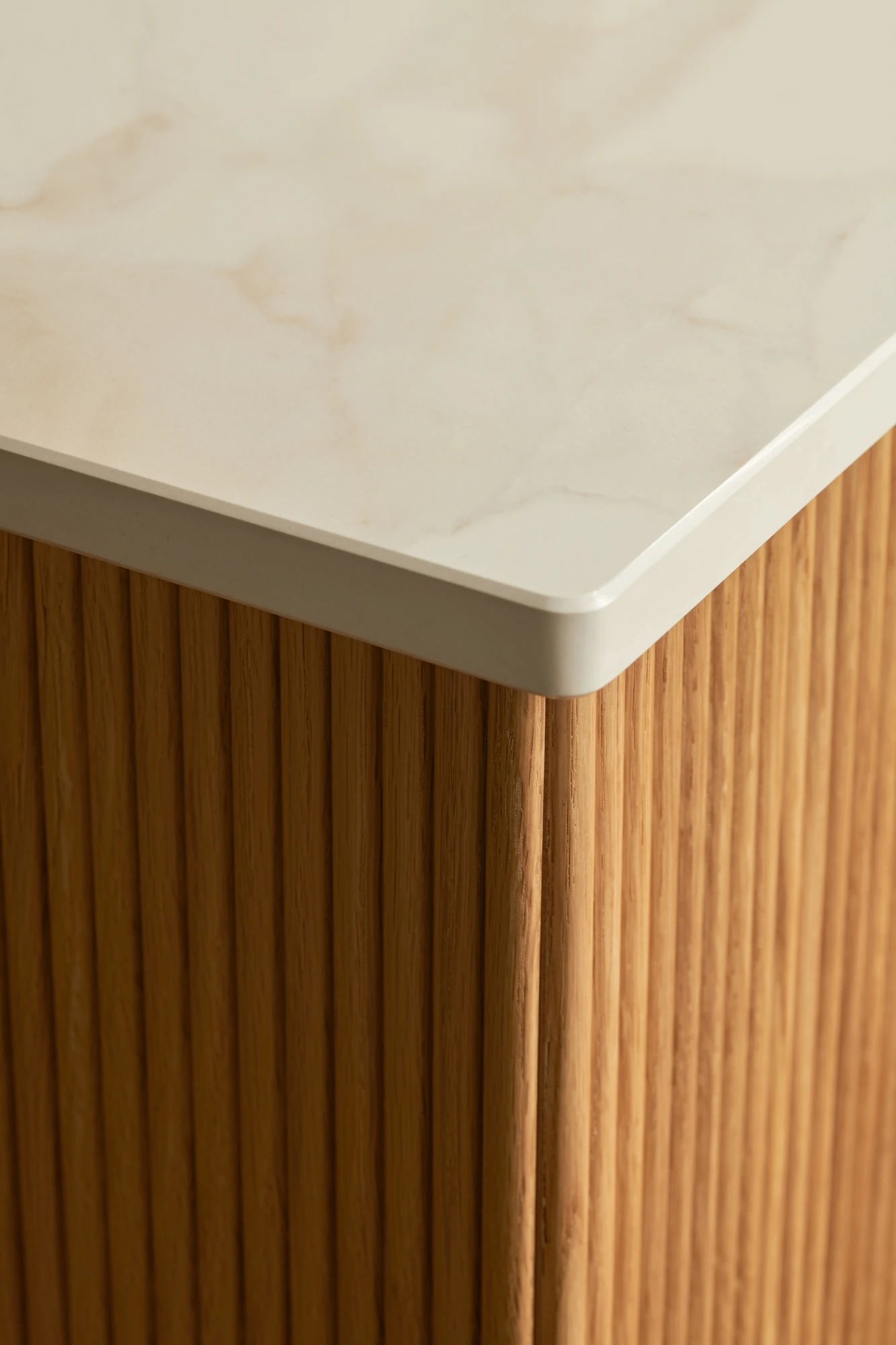 A wooden cabinet with six visible drawers, one of which is slightly open, showing the dovetail joints. The cabinet has a light natural wood finish and a white countertop. The floor partially visible underneath has a colorful patterned rug