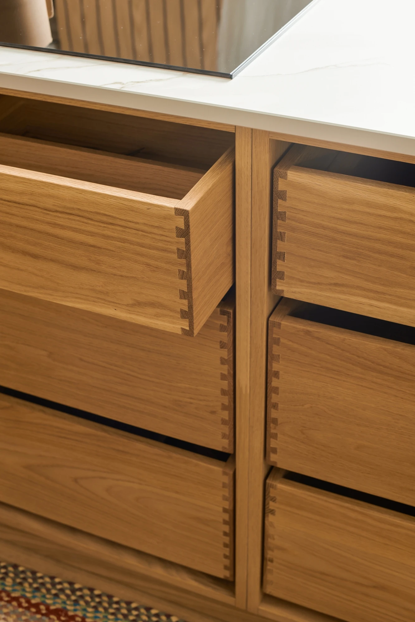 Close-up of a modern wooden corner cabinet with vertical slats, topped with a polished, white marble countertop. The grain of the wood and the smooth surface of the marble create a contrast in textures.