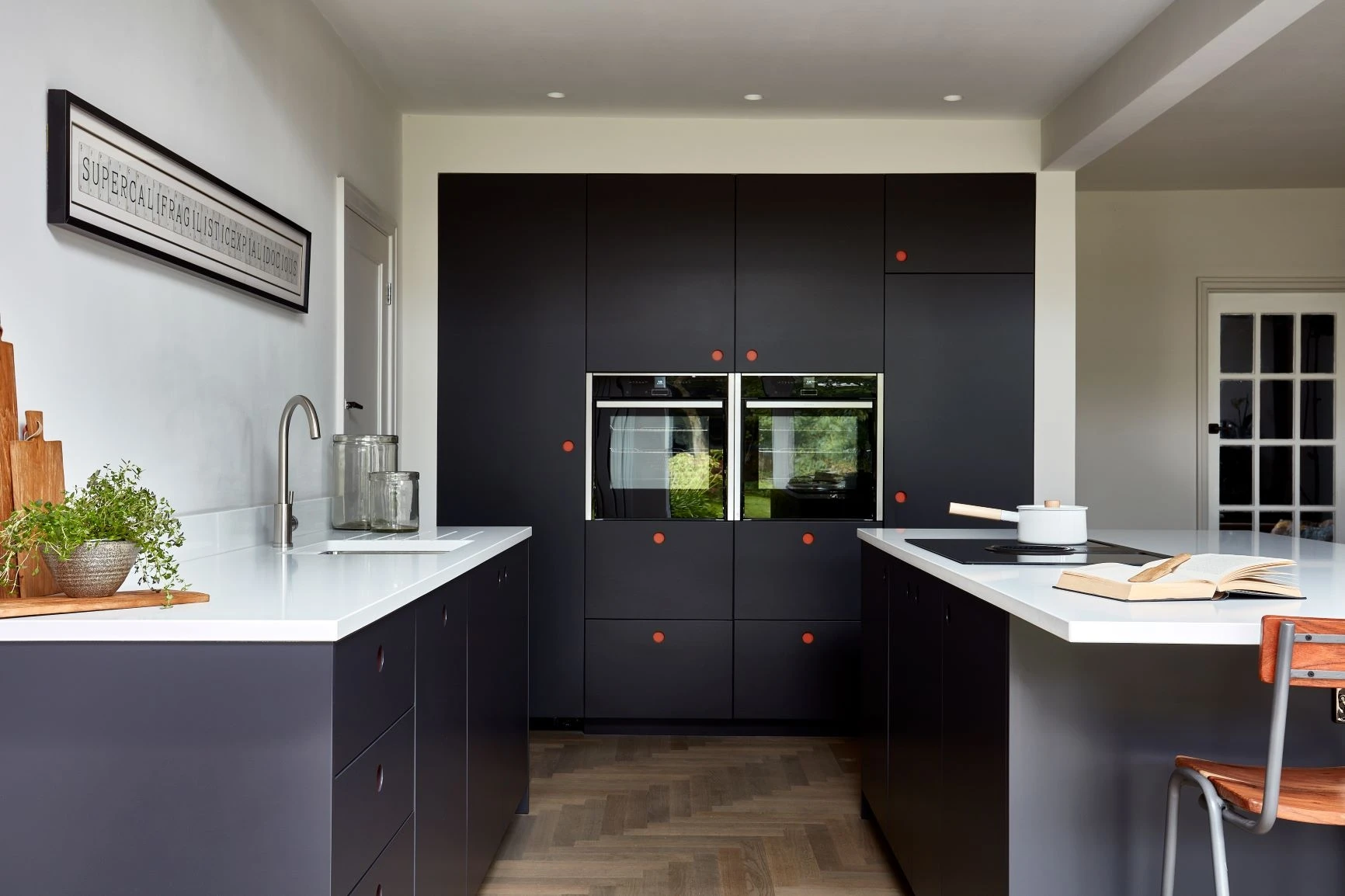 Streamlined blue Ladbroke kitchens with pops of red hardware embrace white quartz surfaces and concealed Miele appliances, promoting a sleek and organized atmosphere.