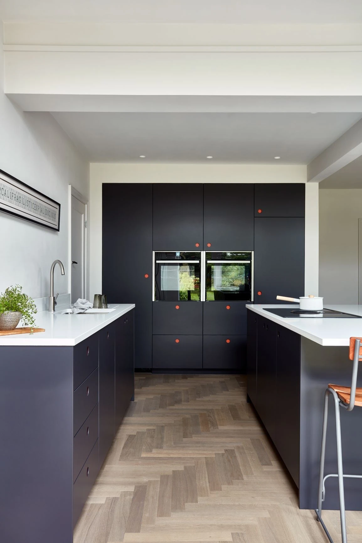 Luxurious blue Ladbroke cabinets with sleek red handles frame expansive white worktops and integrated Miele appliances, inspiring culinary creativity.