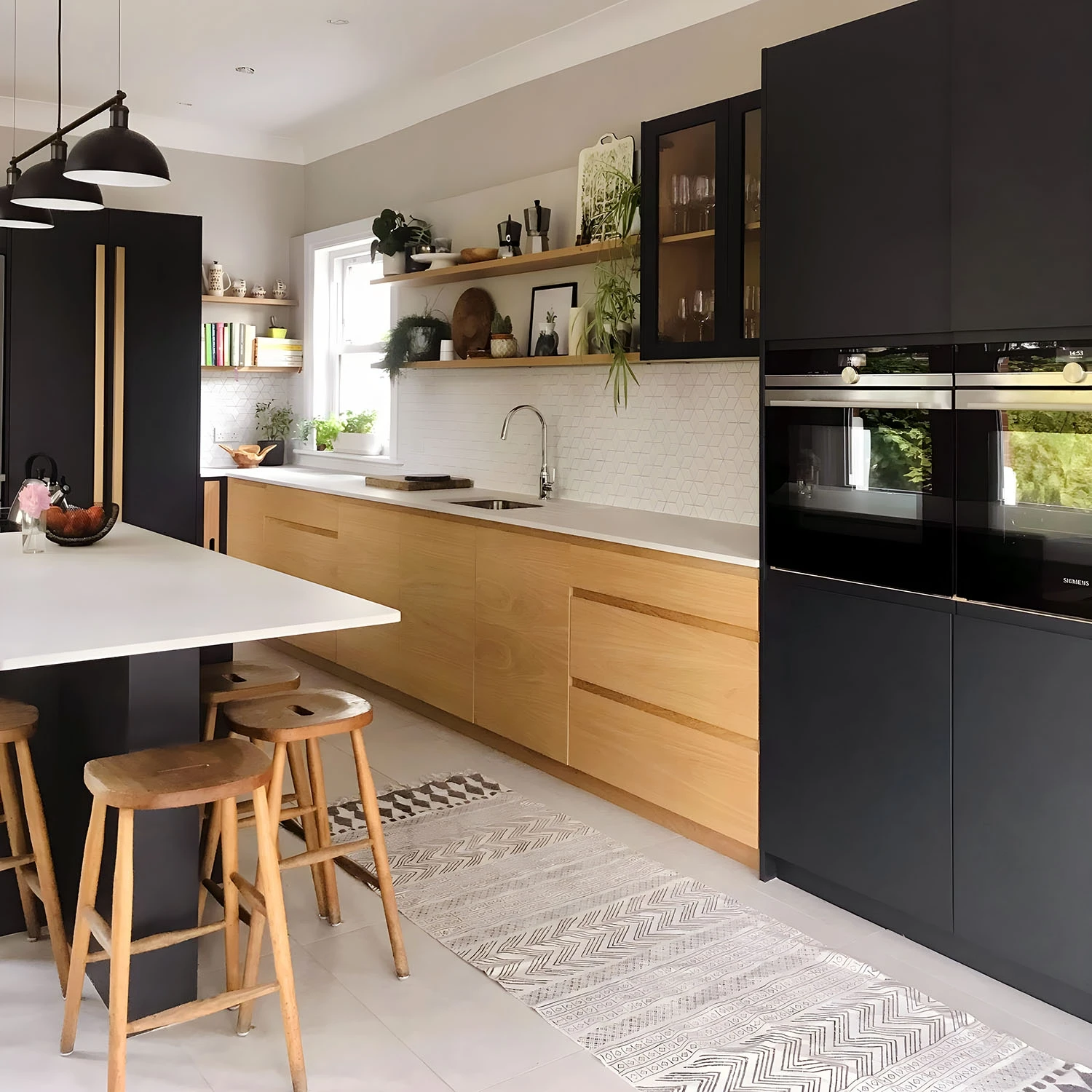 A modern kitchen featuring wooden lower cabinets and matte black upper cabinets. There's a white countertop with a sink and open shelves filled with decor and plants. A kitchen island with wooden stools and hanging pendant lights is in the foreground.