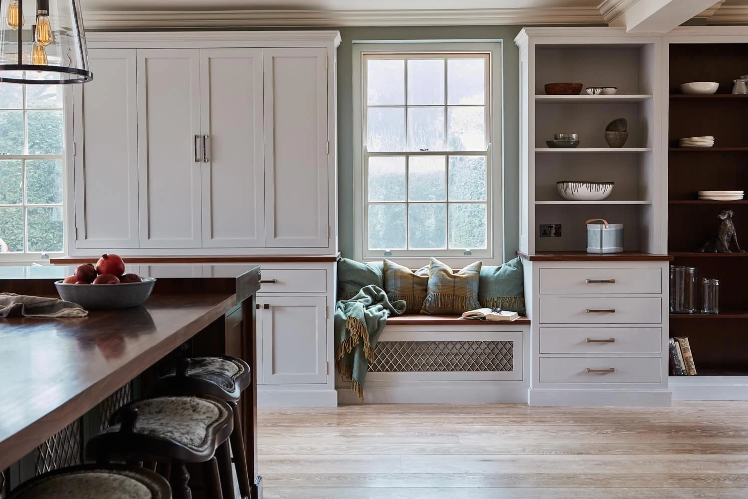 The Georgian Hall kitchen features an expansive layout, which maximises space and functionality. The use of dove grey base cabinets and grain-visible paint finish on the tall Shaker units showcases the natural beauty of the wood.