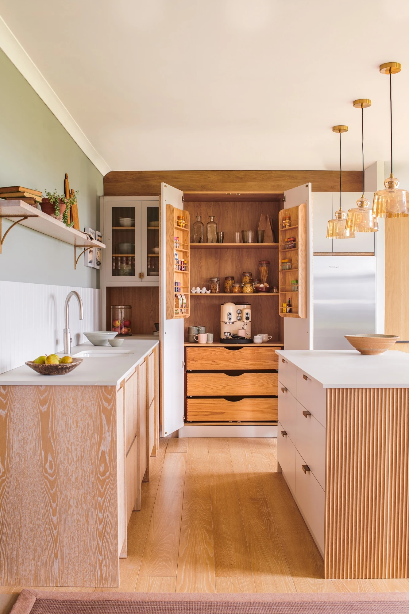 Ample storage solutions abound in this Glaven kitchen, including a tall larder adorned with Norfolk bar handles, generous cabinets, and a large island with ample drawer space, providing ample room for culinary creations and everyday essentials.