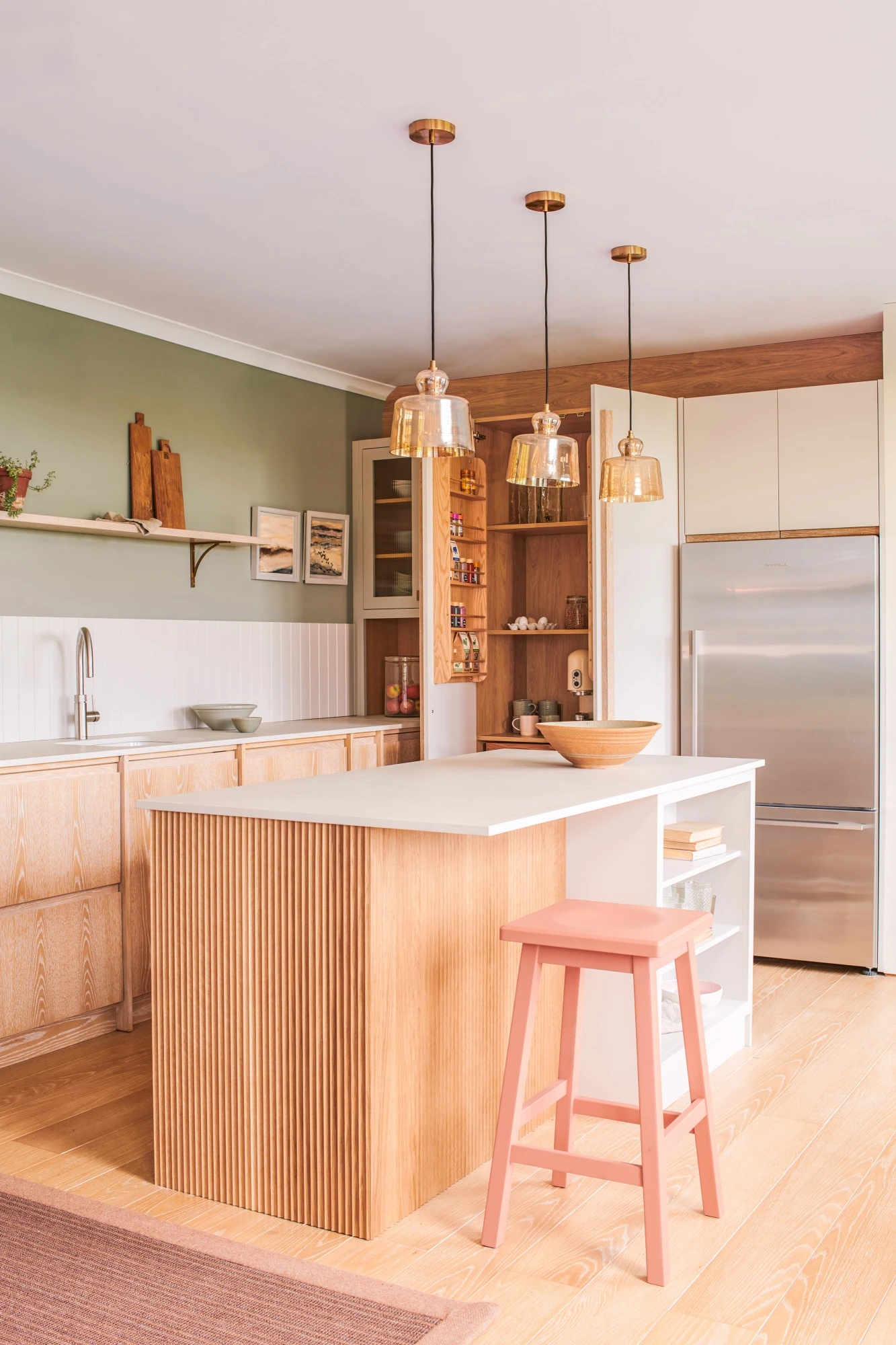 A sense of spaciousness and accessibility is achieved in this Glaven kitchen, with open shelving on the island showcasing personal touches and culinary essentials, while sleek Caesarstone concrete worktops provide a clean and modern backdrop.