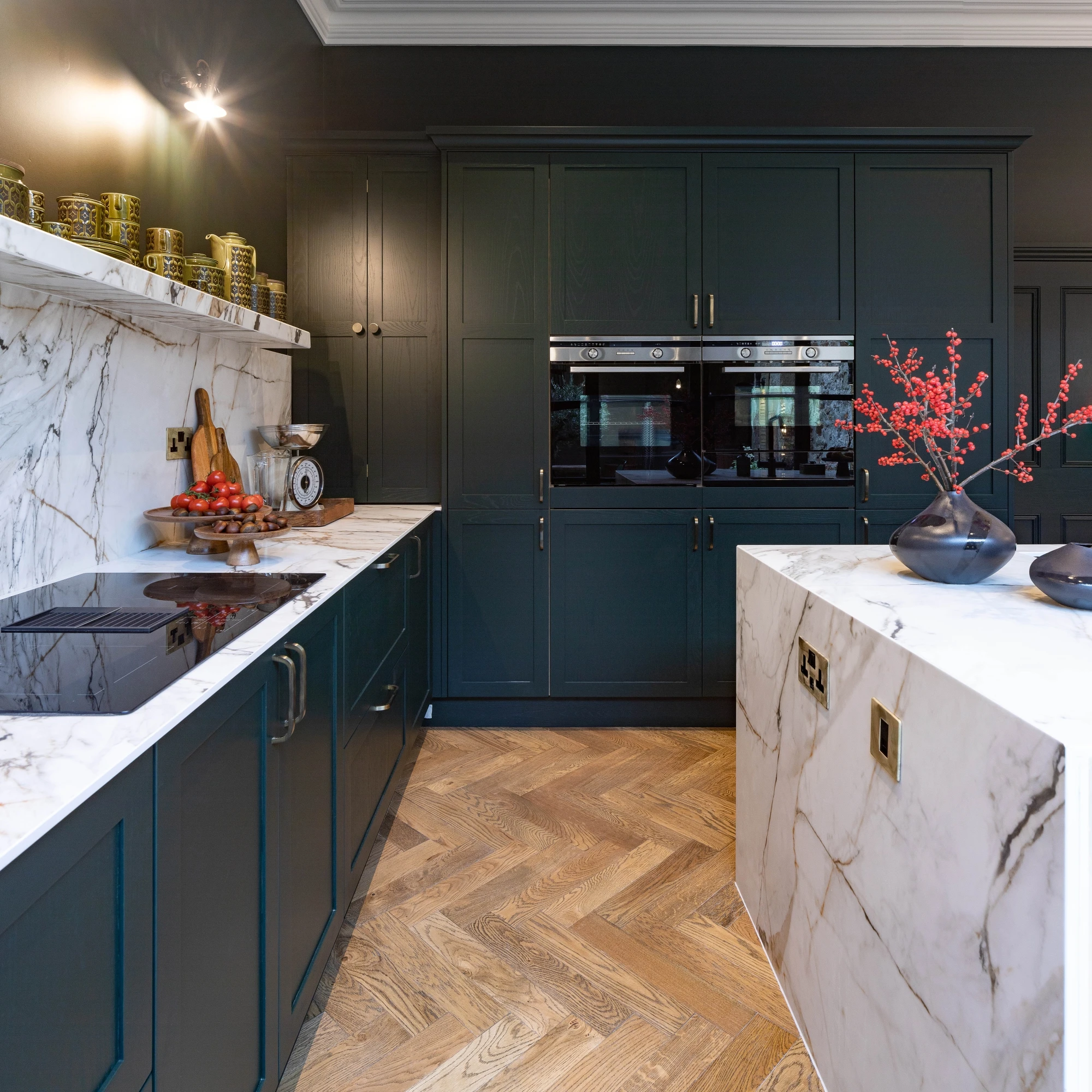 Contemporary kitchen with dark cabinets, marble countertops and backsplash, built-in appliances, and herringbone wooden flooring