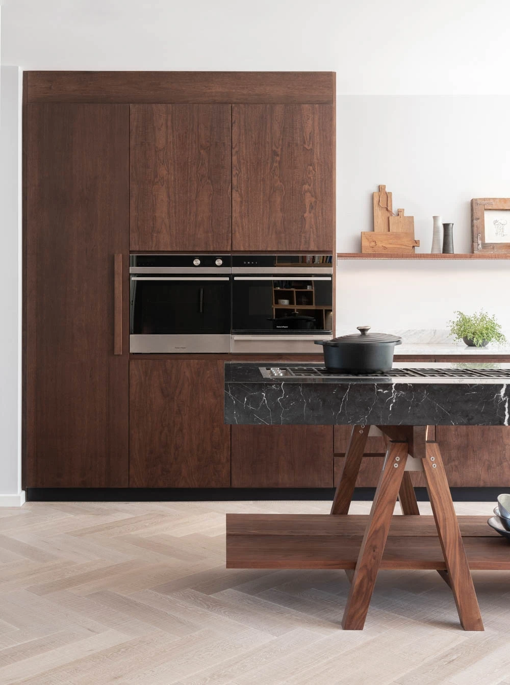 A stunning central island anchors the Highgate kitchen, crafted from a single slab of dark marble, its smooth surface mirroring the countertops. The island's Walnut frame complements the cabinetry, creating a cohesive and elegant design.