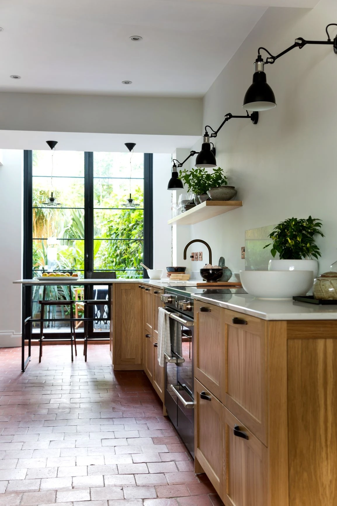 The garden outside becomes part of the kitchen experience through Crittal doors, with exposed oak fronts echoing the vibrant greenery.