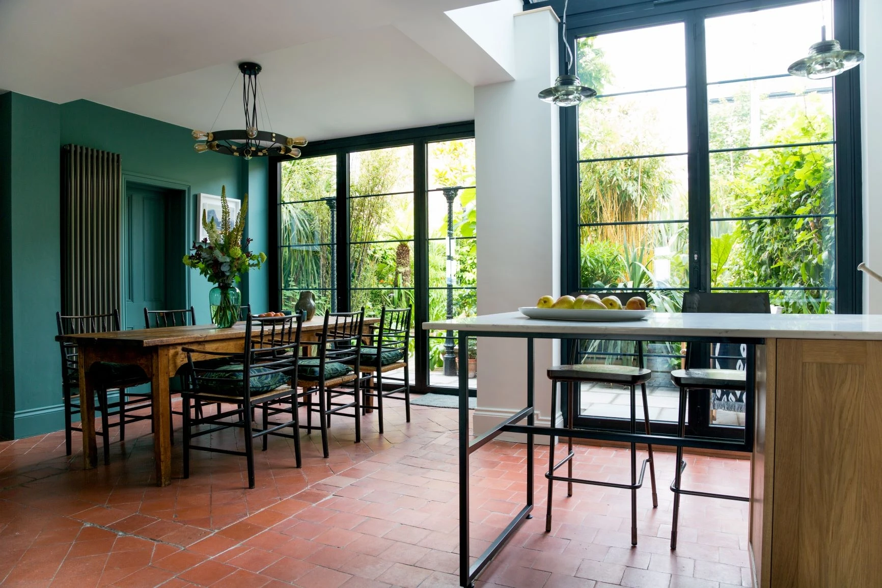 Dark dining table ties in with black bronze details throughout the kitchen, adding a pop of color against smooth green paint.