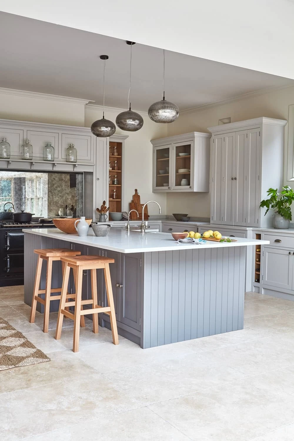 Captivating view of the Norfolk Vicarage kitchen, featuring sleek Shaker-style cabinets in a warm white hue, gleaming Carrara quartz worktops. The generous island anchors the kitchen, offering ample countertop space, a seating area, and a built-in cocktail corner.