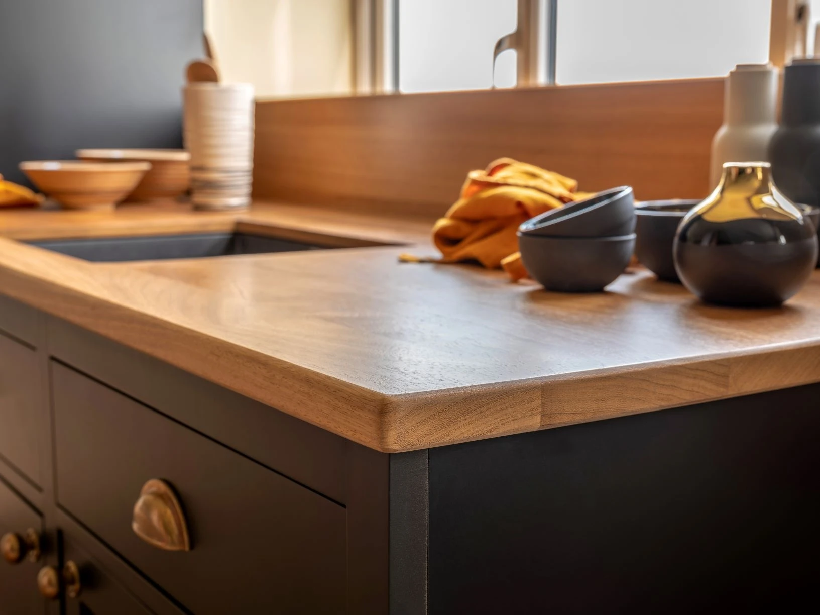 Warmth radiates from the oak worktop as it seamlessly meets the smooth black doors, creating a mesmerizing interplay of textures and adding depth to the minimalist design.