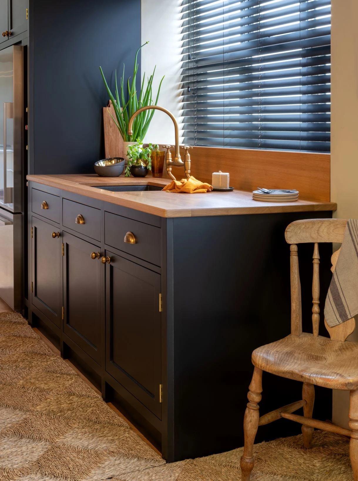 Picture-perfect black painted cabinets adorned with gleaming brass hardware set the stage for a luxurious coastal kitchen, bathed in natural light from expansive windows