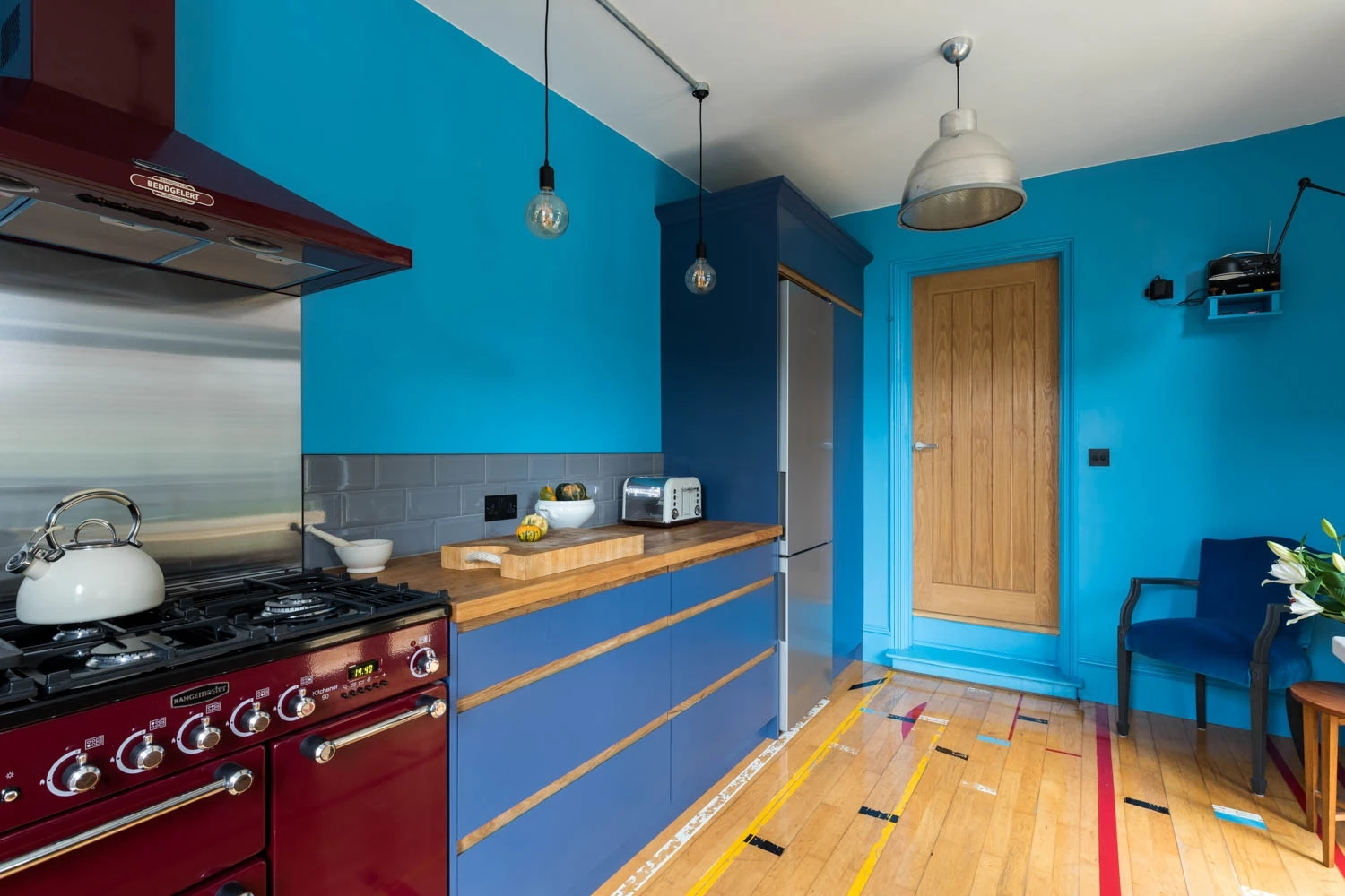 Vibrant red Rangemaster pops against the serene depth of blue J-groove cabinetry, a symphony of color that defines modern sophistication in the kitchen.