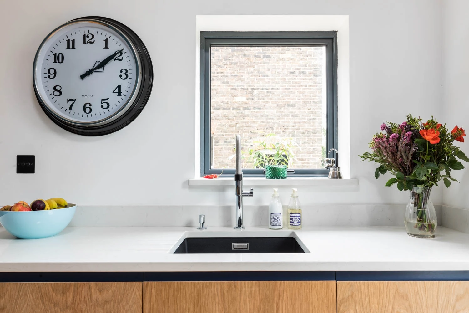 Quartz white countertops embrace the natural warmth of oak J-groove cabinets, bathed in natural light and infused with a touch of floral delight, for a kitchen that's both modern and inviting.