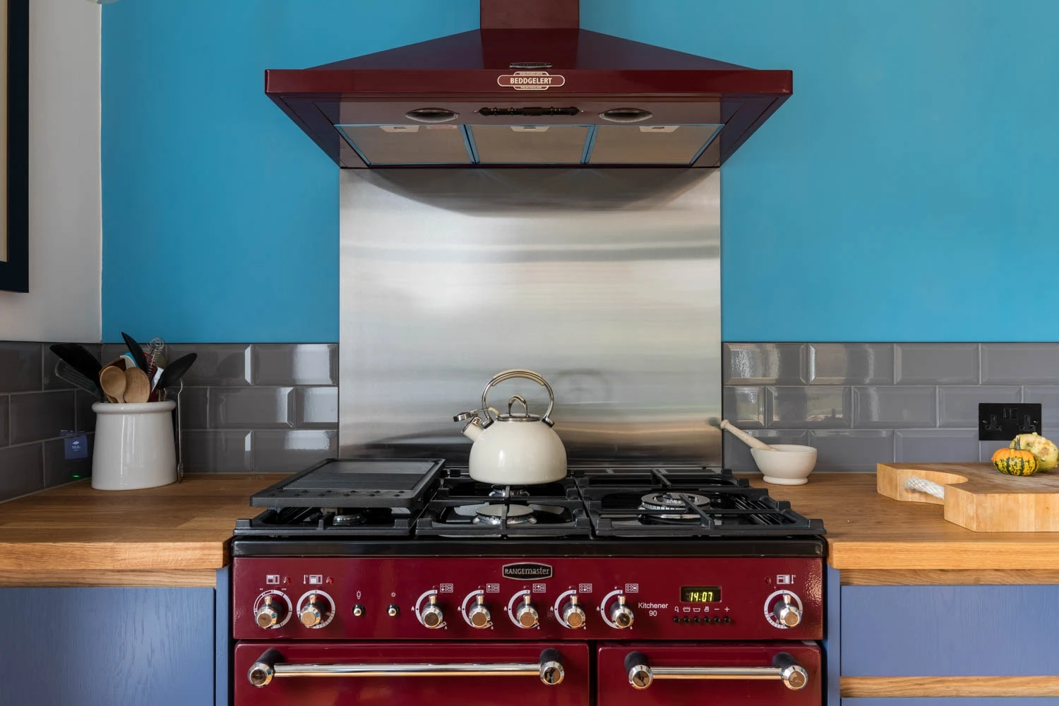 Gleaming red Rangemaster ignites a passion for cooking, poised above timeless blue J-groove cabinets, a symphony of modern functionality and classic elegance.