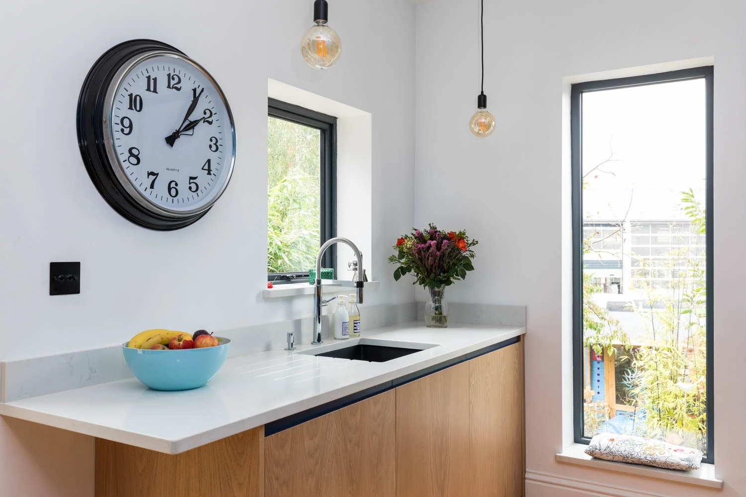 Crisp quartz white worktop shimmers above earthy oak J-groove cabinets, bathed in natural light from a sunlit window.