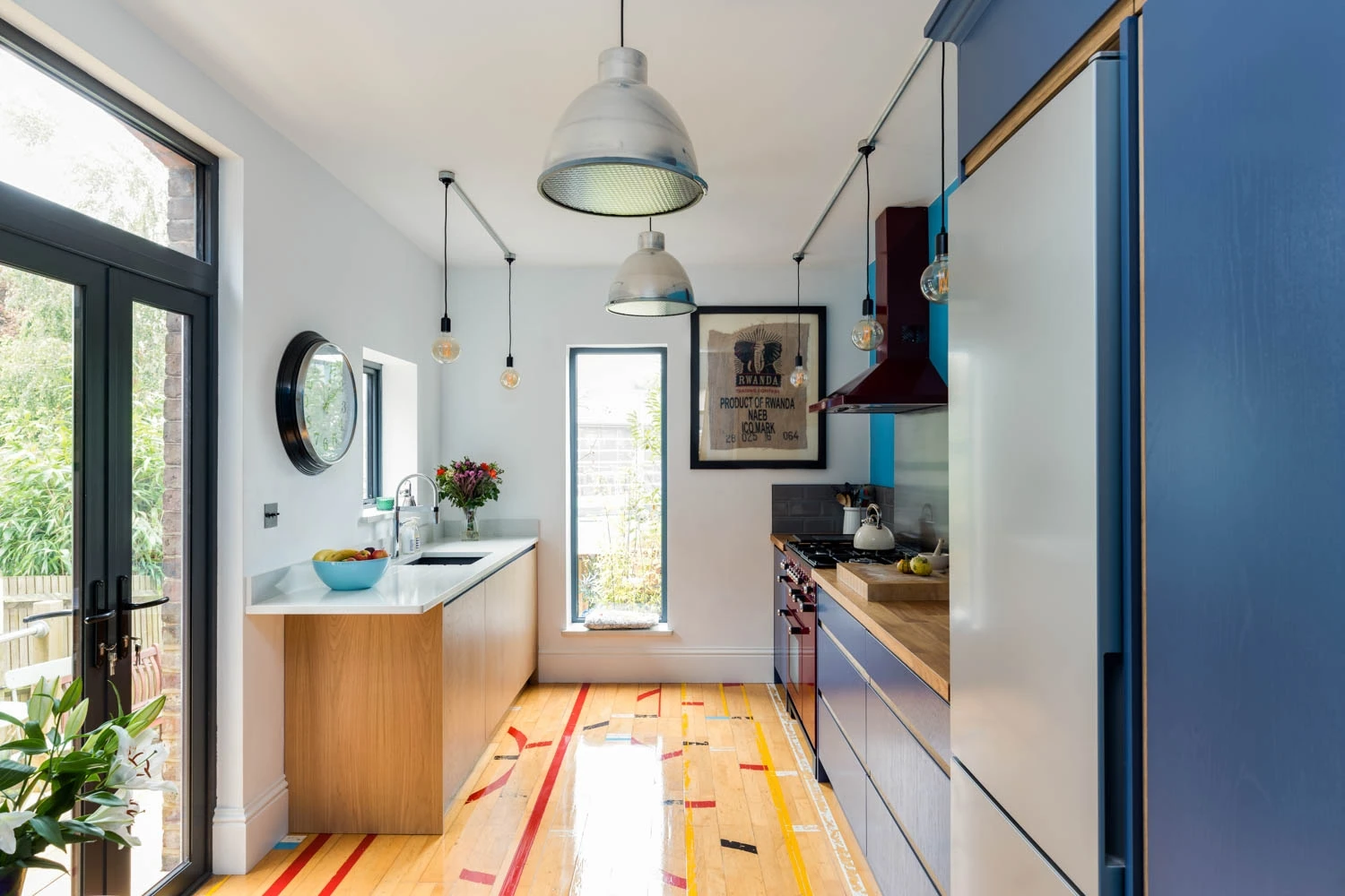 Embrace tranquility in this kitchen where tranquil blue cabinets meet airy white surfaces, all under the watchful gaze of a towering window revealing nature's wonders.