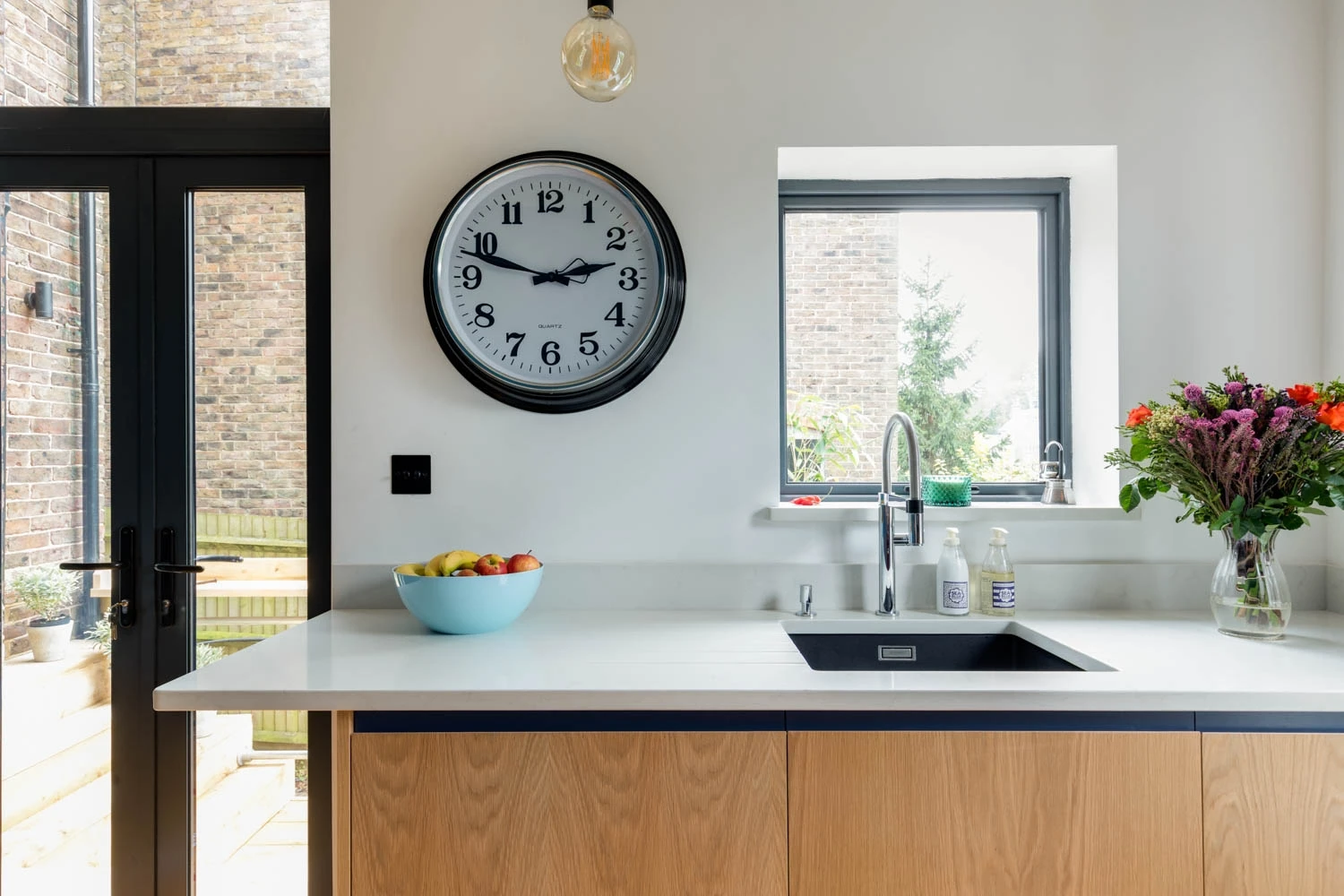 Inviting quartz white countertops and warm oak J-groove cabinetry create a calming haven, illuminated by natural light and accented with a touch of floral charm.