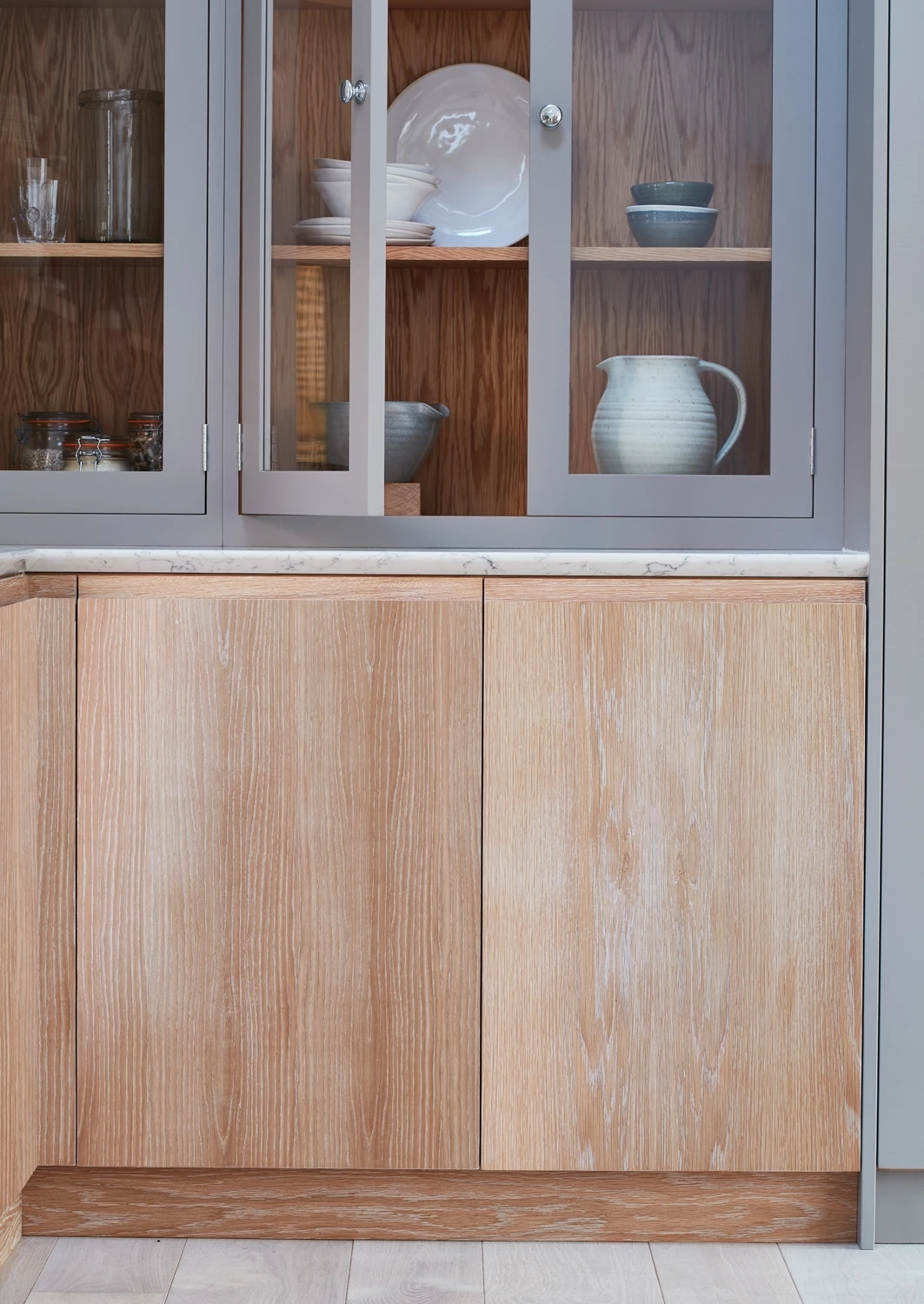 Walnut and grey kitchen with j-groove doors and some glazed wall cabinetry. A central island has v-groove paneling under the walnut worktop