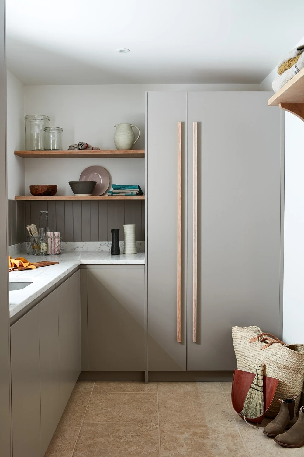 Walnut and grey kitchen with j-groove doors and some glazed wall cabinetry. A central island has v-groove paneling under the walnut worktop