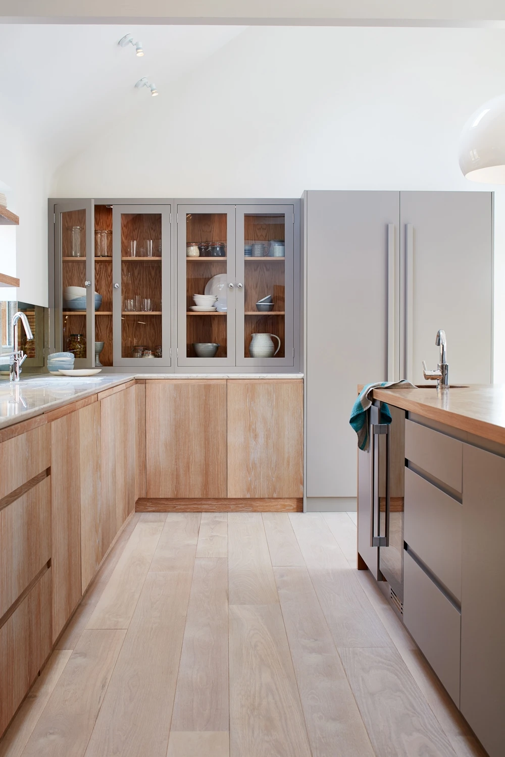 Walnut and grey kitchen with j-groove doors and some glazed wall cabinetry. A central island has v-groove paneling under the walnut worktop